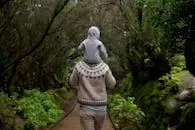 A father carrying his child on a forest path, enjoying nature and bonding on an autumn day.
